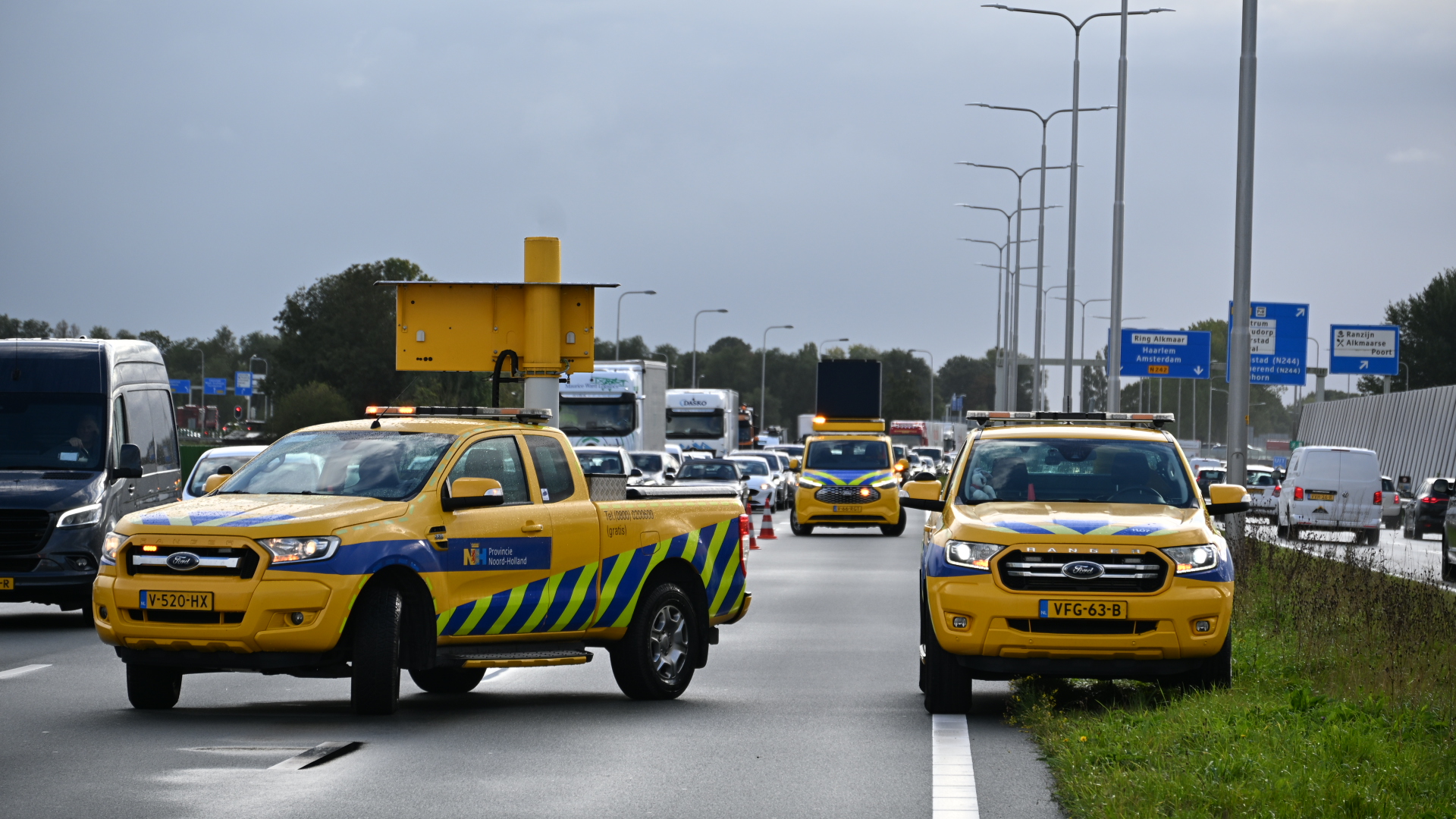 Gele weginspectievoertuigen met knipperlichten op drukke snelweg, met pijlwagen en afzetkegels in de verte