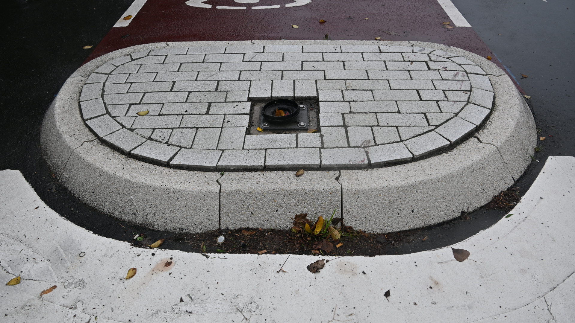 Verhoogd rond plateau met witte klinkers en een verzonken lamp in het midden, op een nat wegdek met bladeren
