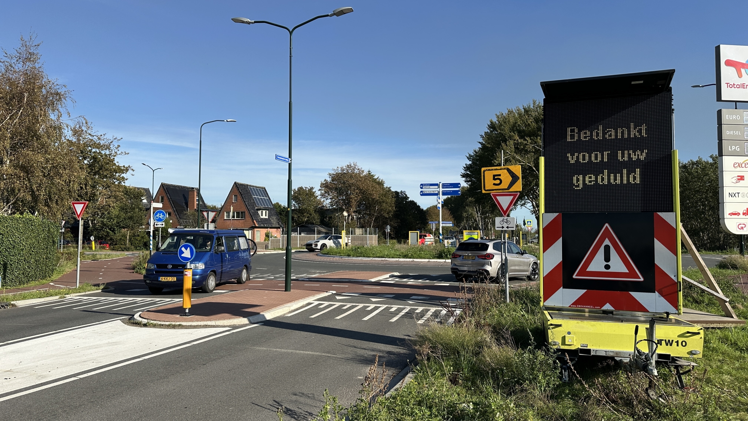 Matrixbord bij rotonde met tekst Bedankt voor uw geduld en waarschuwingsdriehoek, met passerende auto’s