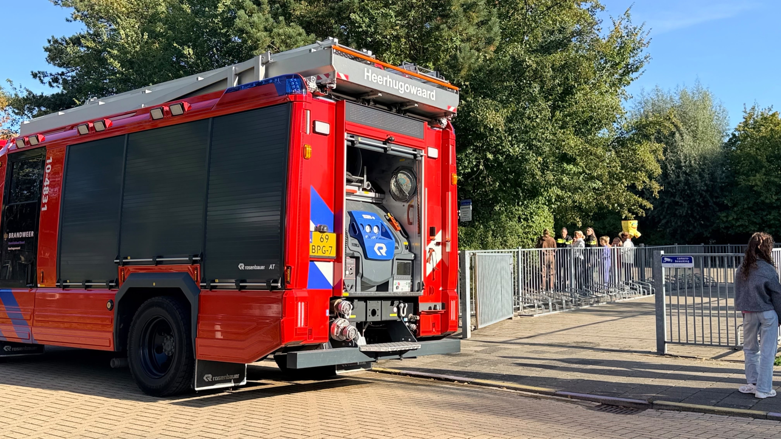 Rode brandweerwagen van Heerhugowaard met open achterklep en apparatuur, geparkeerd bij hek met omstanders