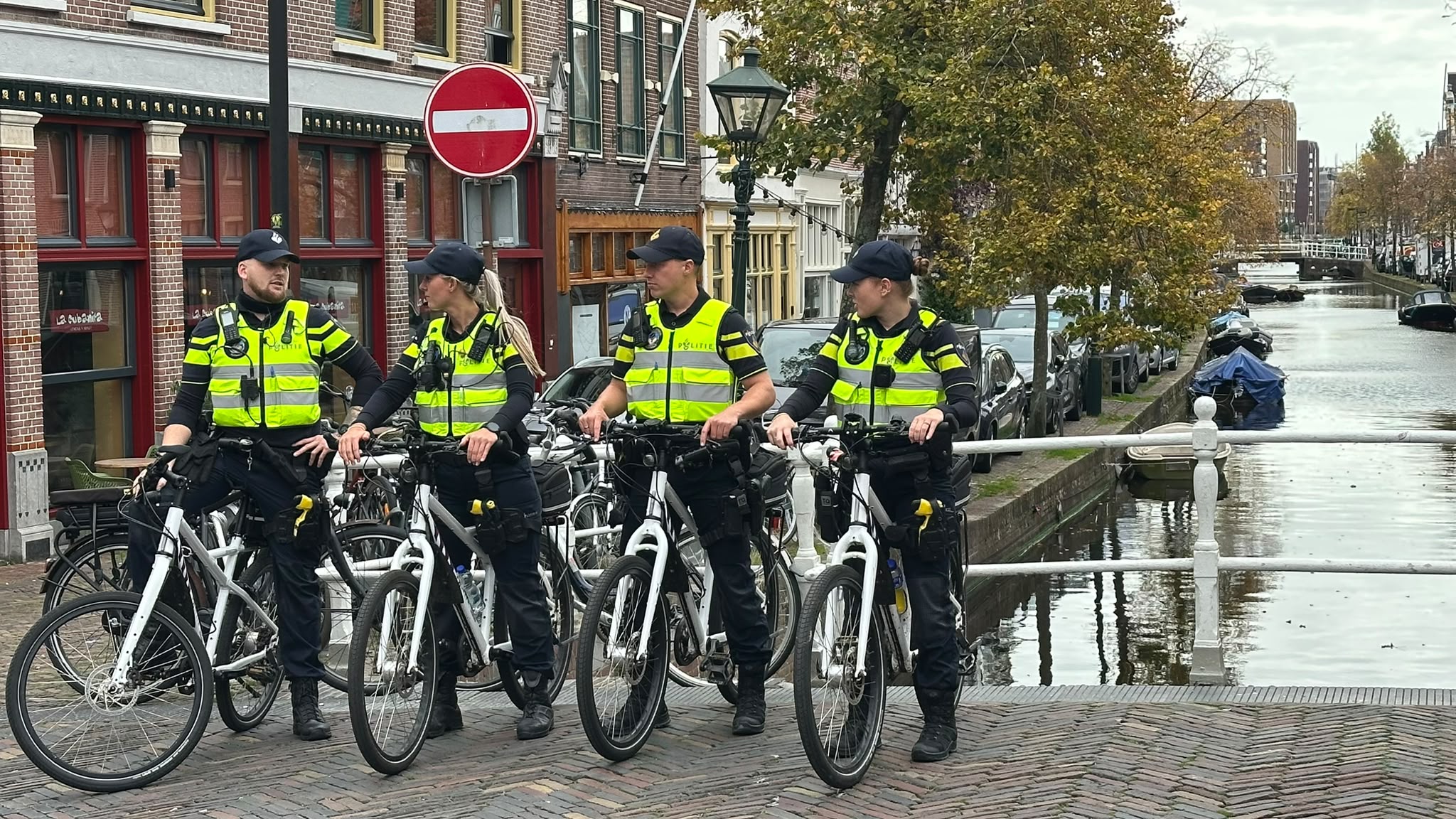 Vier agenten van de Nederlandse politie op fietsen op een brug bij een gracht, met een rood verboden-inrijdenbord