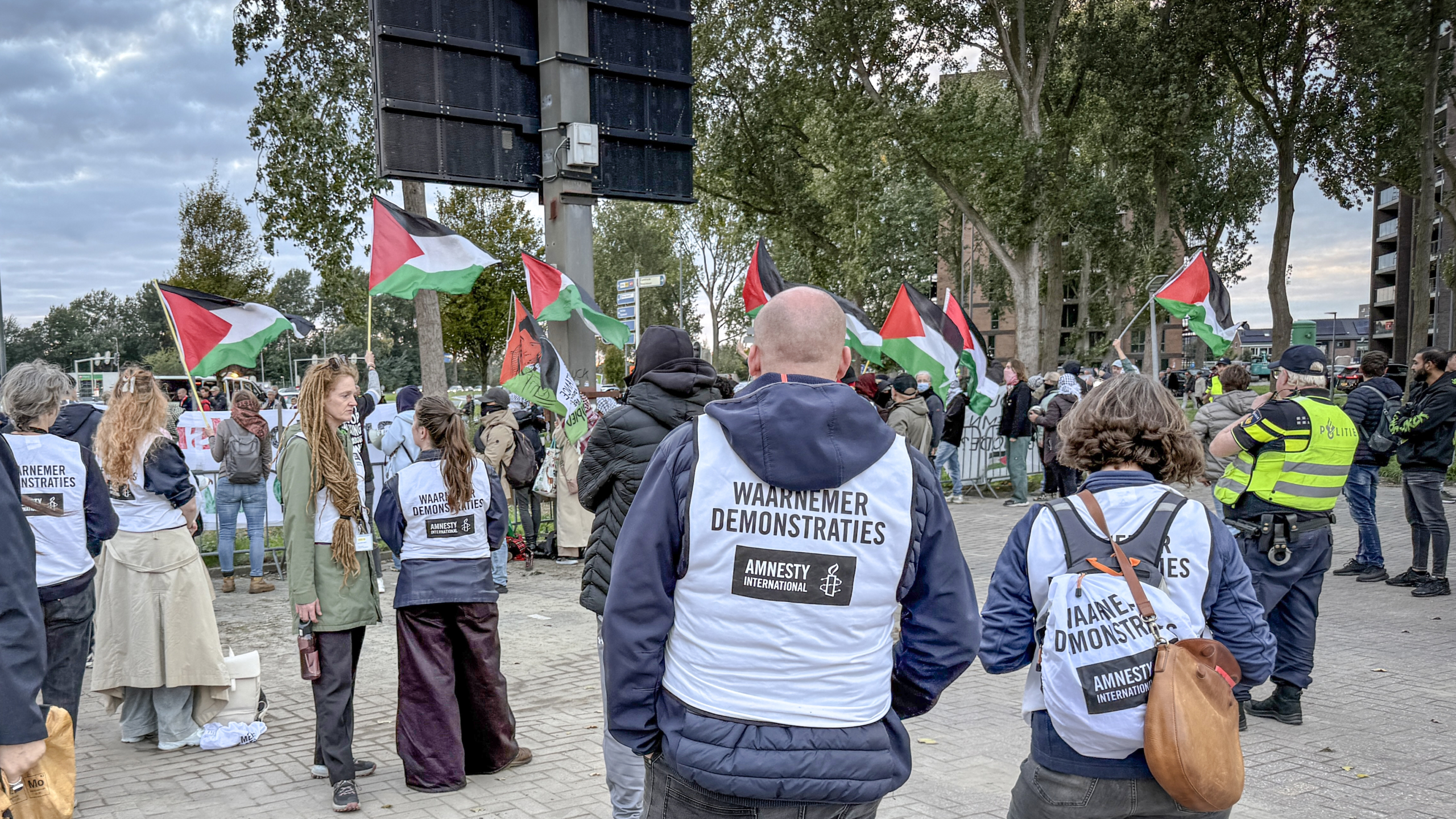 Demonstratie met Palestijnse vlaggen; waarnemers van Amnesty International in hesjes en politie op de achtergrond