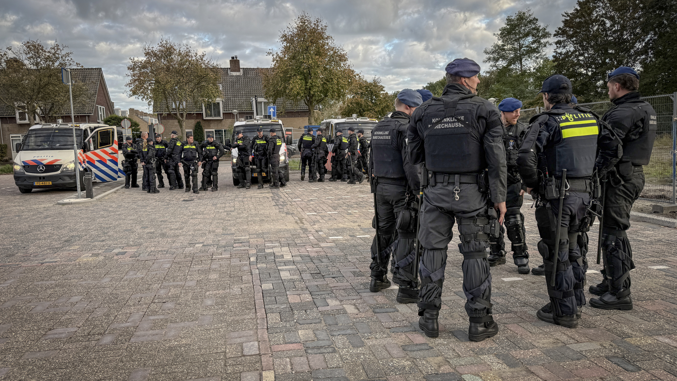 Groep politieagenten en marechaussees in oproeruitrusting bij politiebusjes in een woonwijk
