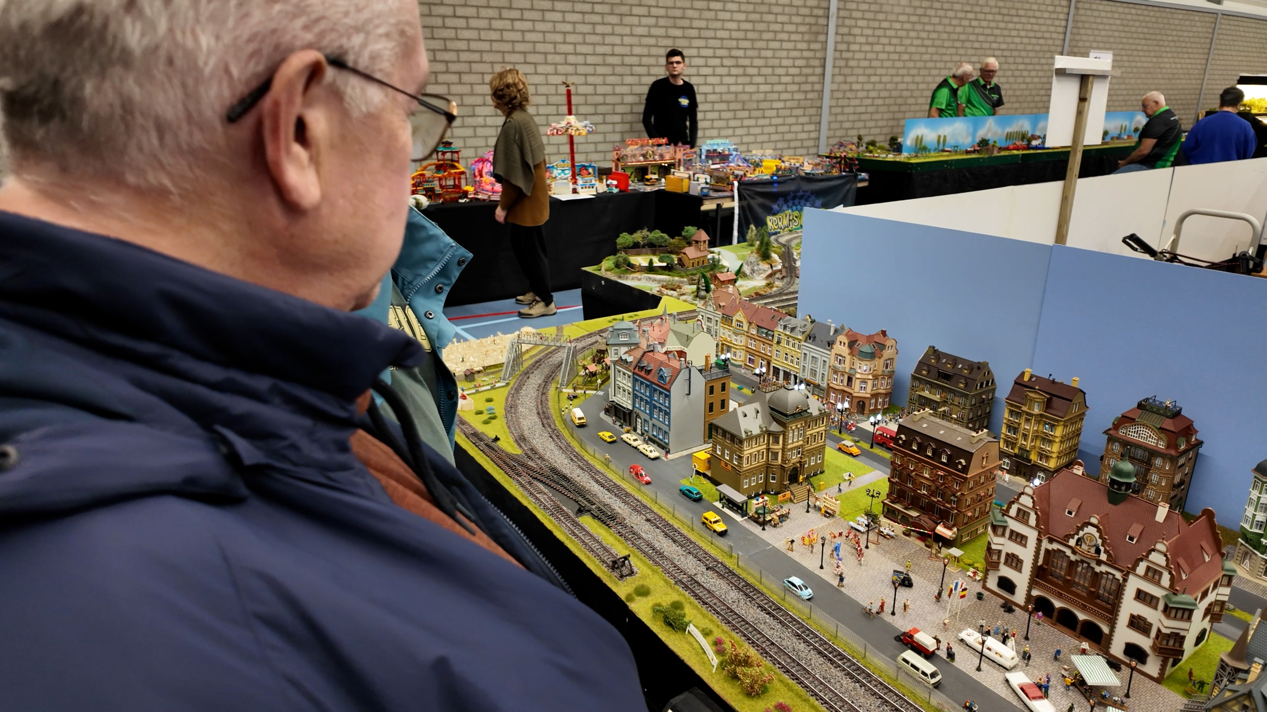 Bezoeker bekijkt een modelspoorbaan met miniatuurstad, treinrails en druk straatbeeld in een expositiehal