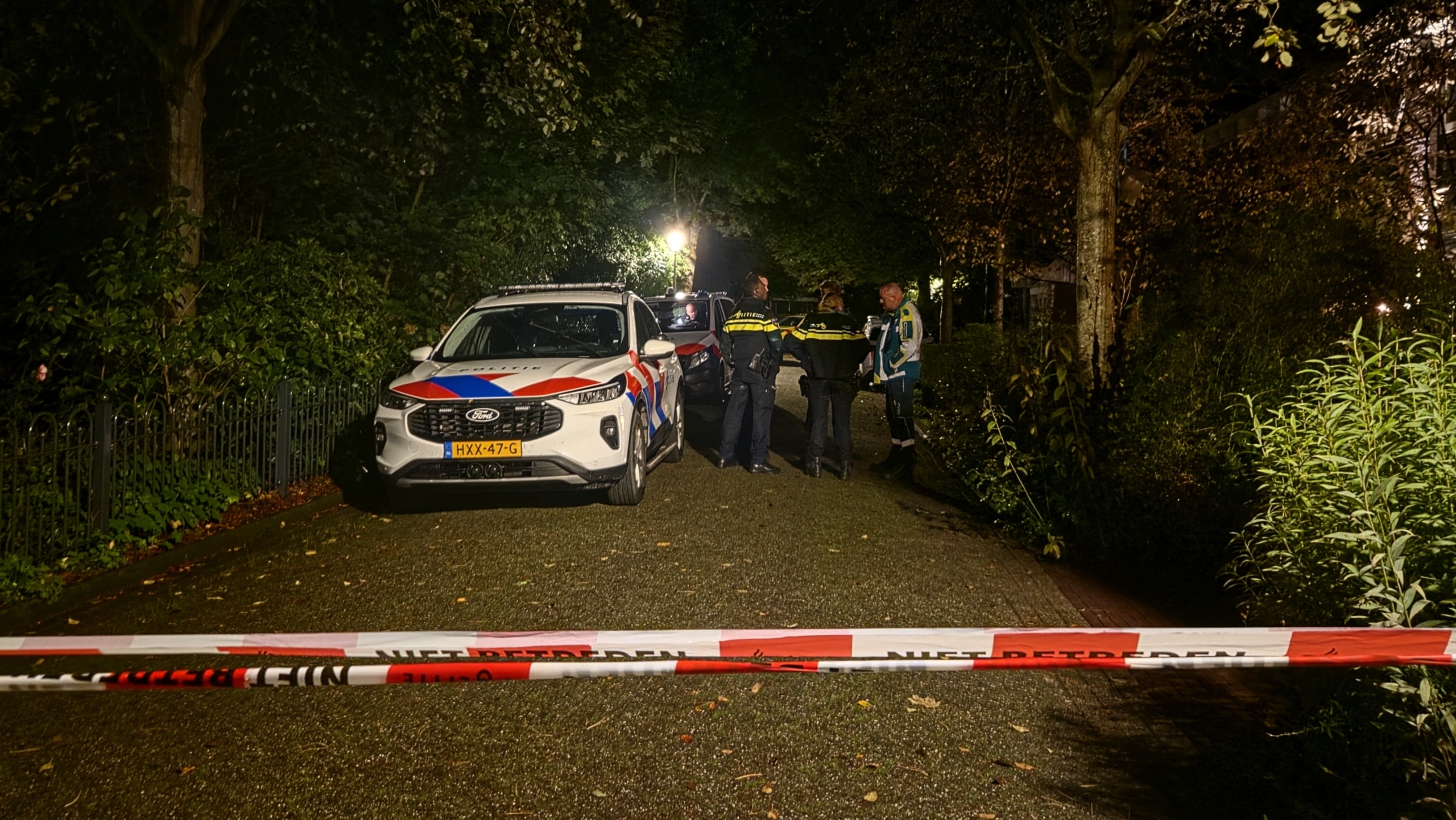 Politieauto en agenten op een donker bospad achter rood-wit lint met tekst ‘NIET BETREDEN’