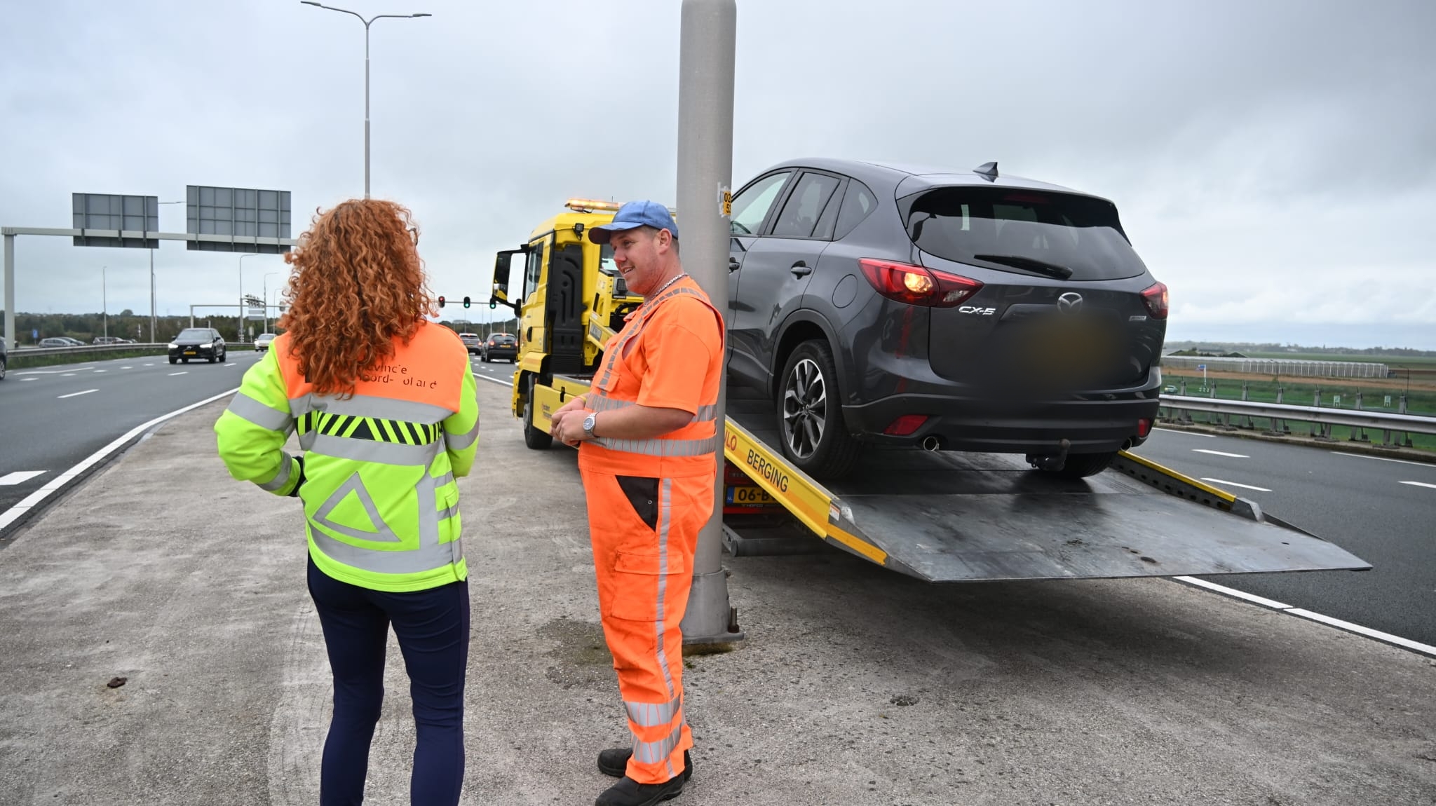 Bergingsmedewerker en weginspecteur praten langs de snelweg bij auto op een oprijwagen
