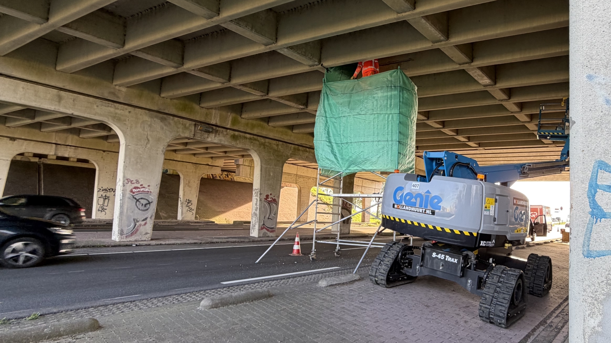 Hoogwerker onder viaduct bij wegwerkzaamheden, met steiger en groen afdekzeil rondom werkplek