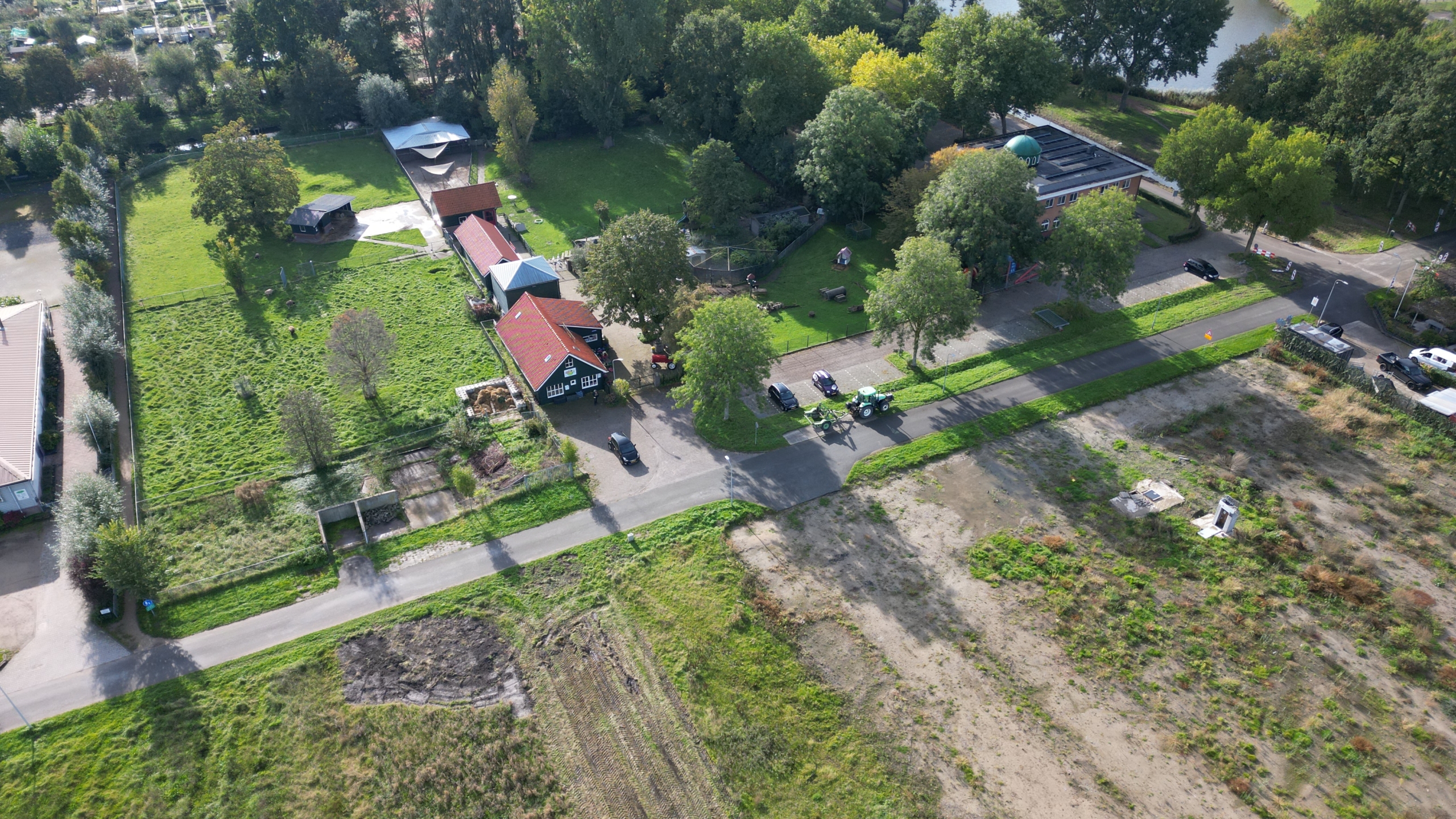 Luchtfoto van boerderijcomplex met rode daken, weiland met bomen en weg met auto’s en tractor