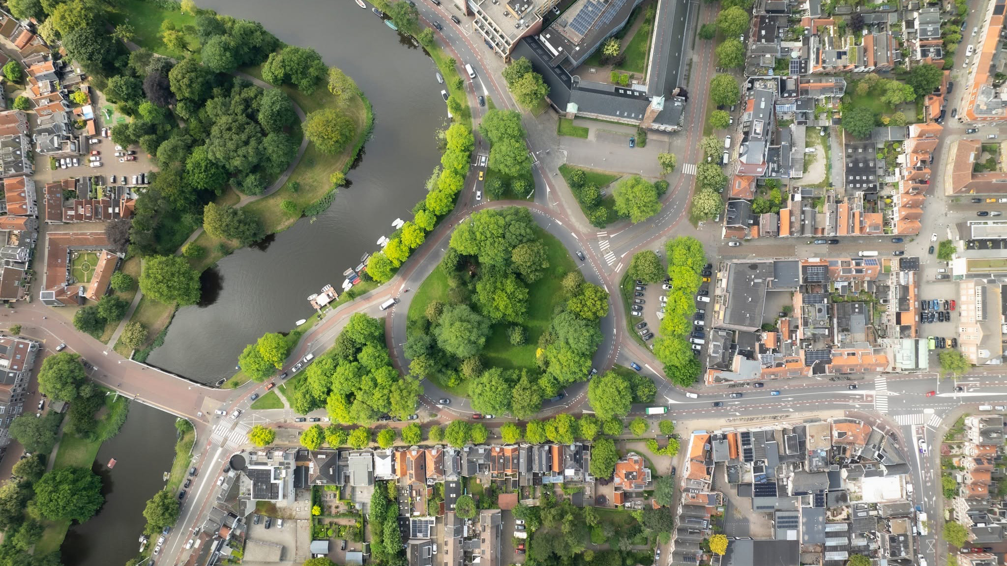 Luchtfoto van stadswijk met rivier, ronde rotonde in een groen park en omliggende straten met huizen en verkeer