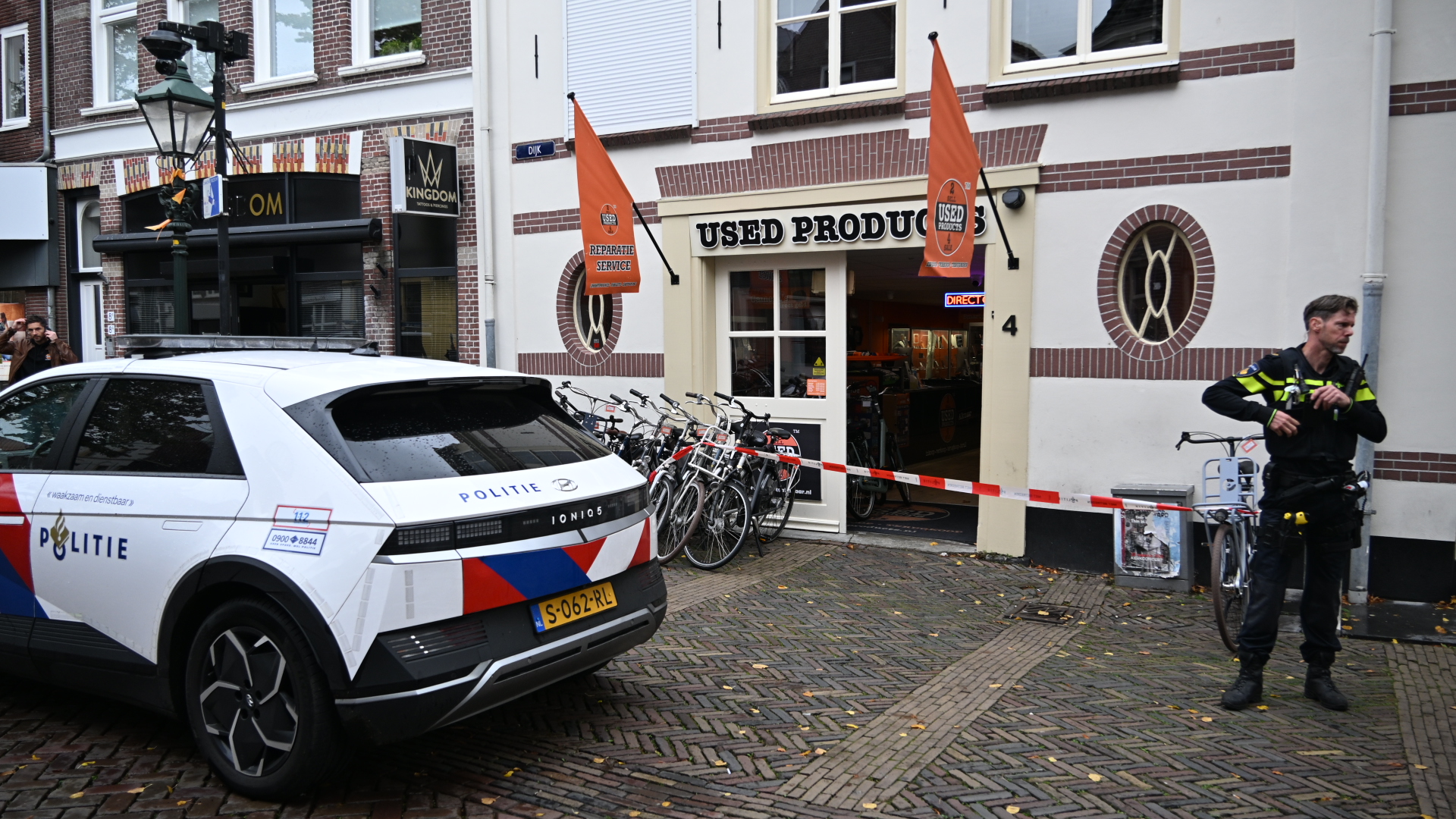 Politieauto en agent bij met lint afgezet winkelpand “Used Products”, met fietsen voor de ingang