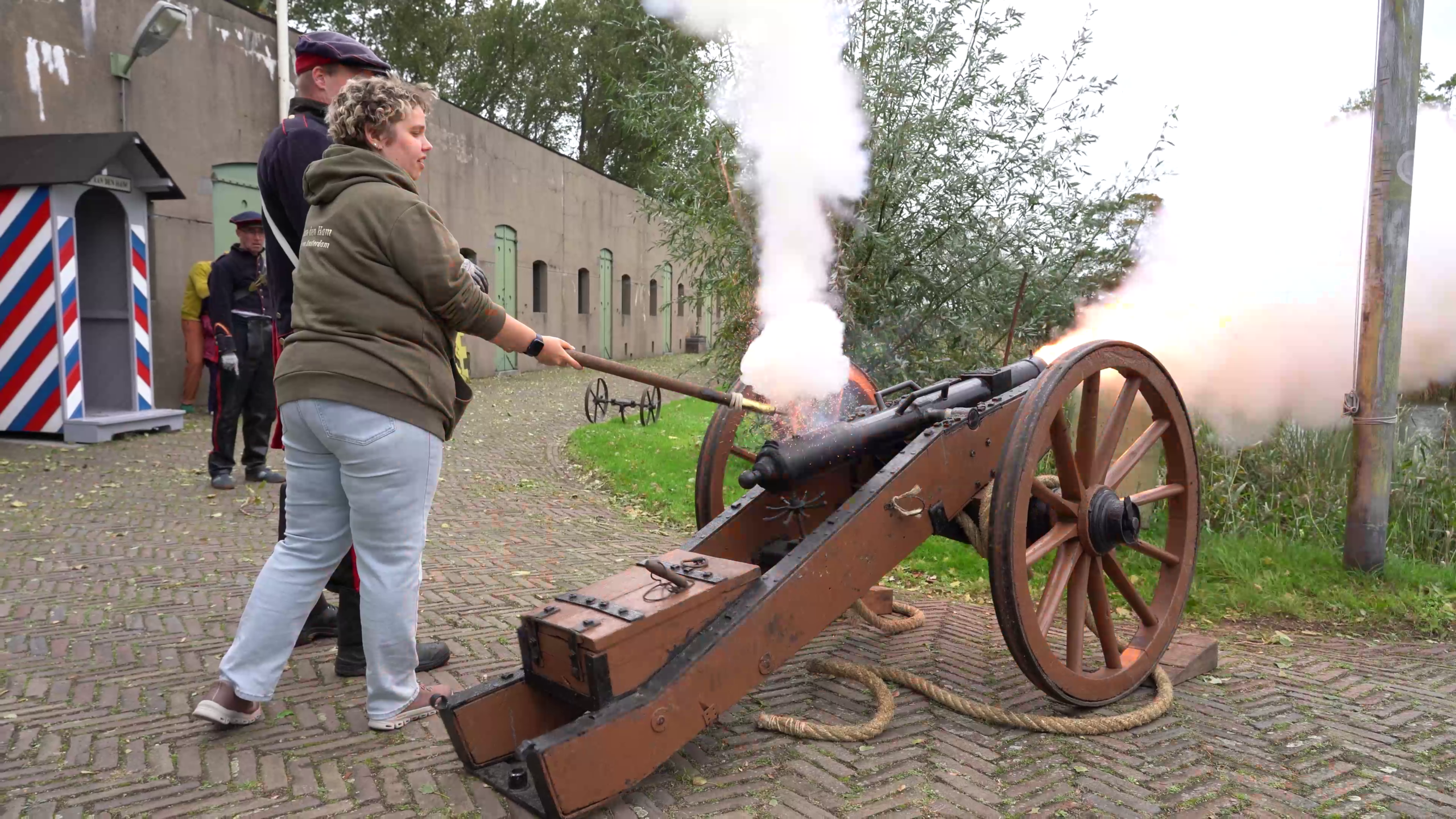 Persoon steekt een historisch kanon aan met een lont, terwijl rook en vlammen uit de loop komen