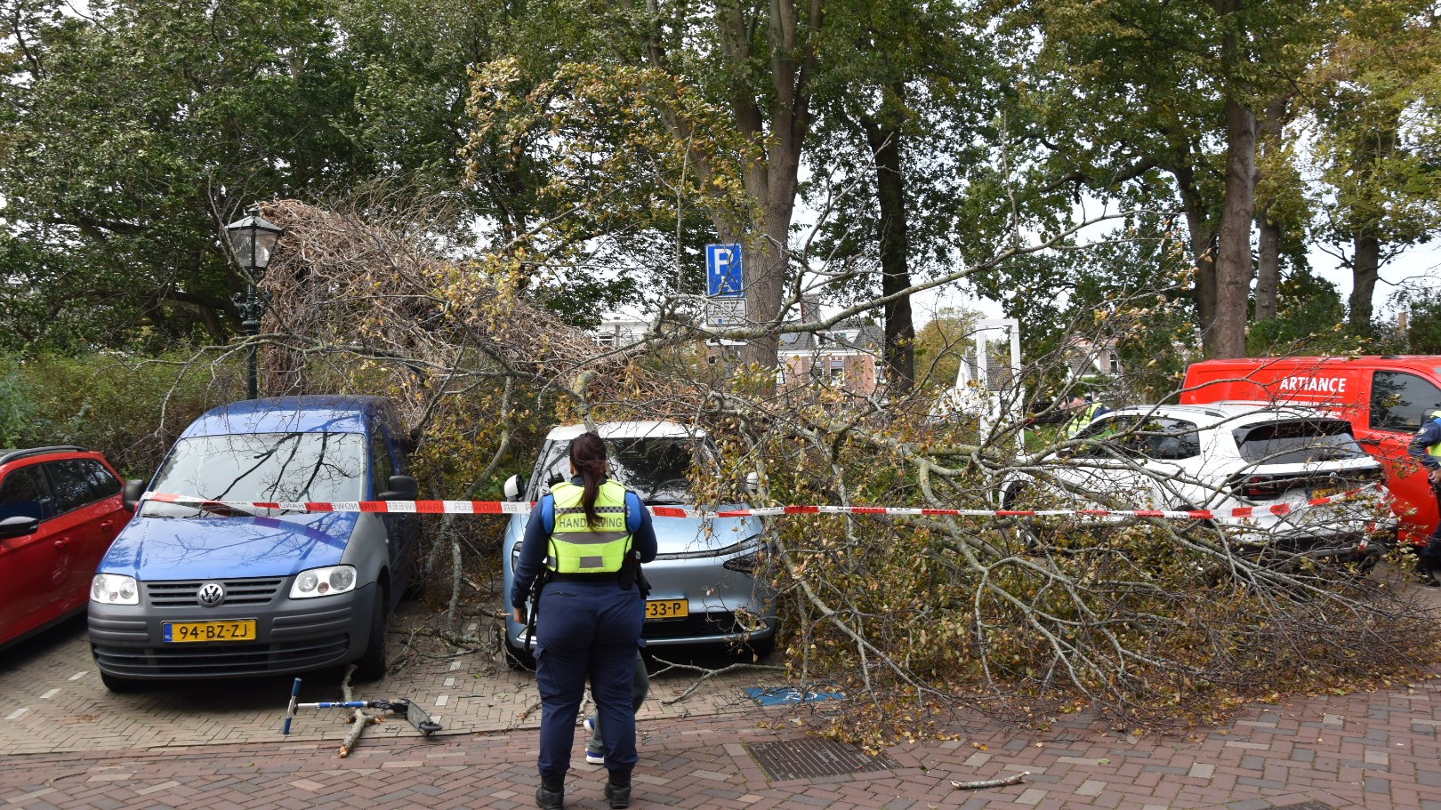 Handhaver staat bij met lint afgezet parkeerterrein waar een omgevallen boomtak op auto’s is gevallen