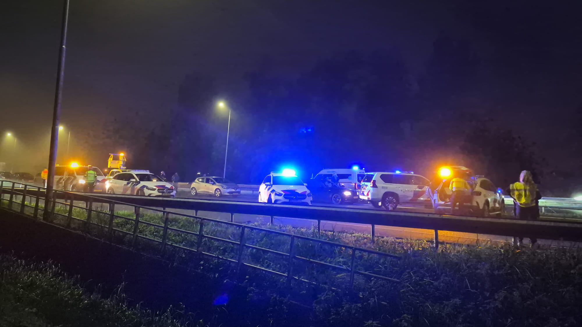 Politie- en hulpverleningsvoertuigen met zwaailichten bij een incident op een snelweg in het donker