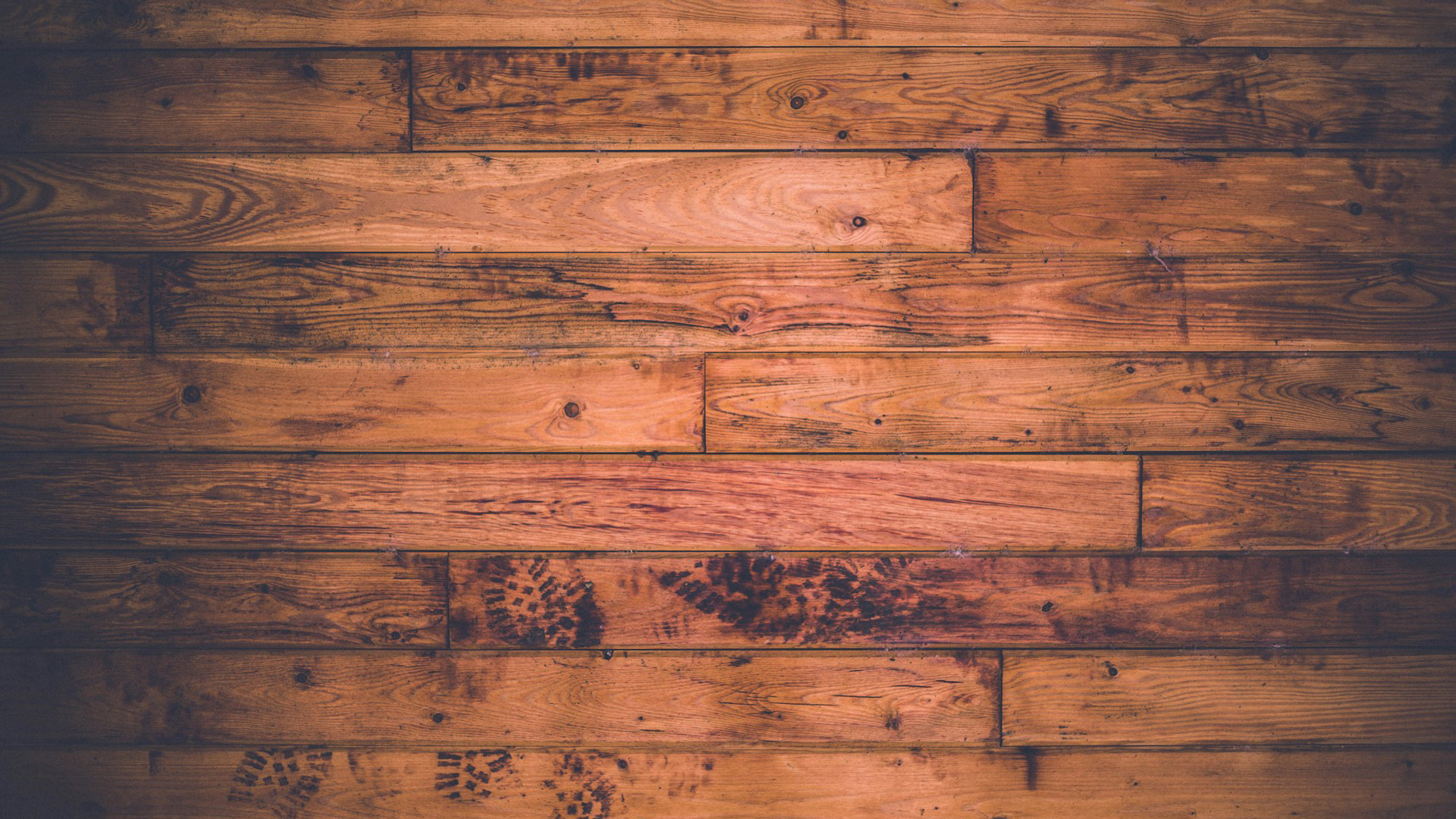 Houten plankenwand met warme bruine tinten, duidelijke houtnerven en donkere vlekken zoals schoenafdrukken