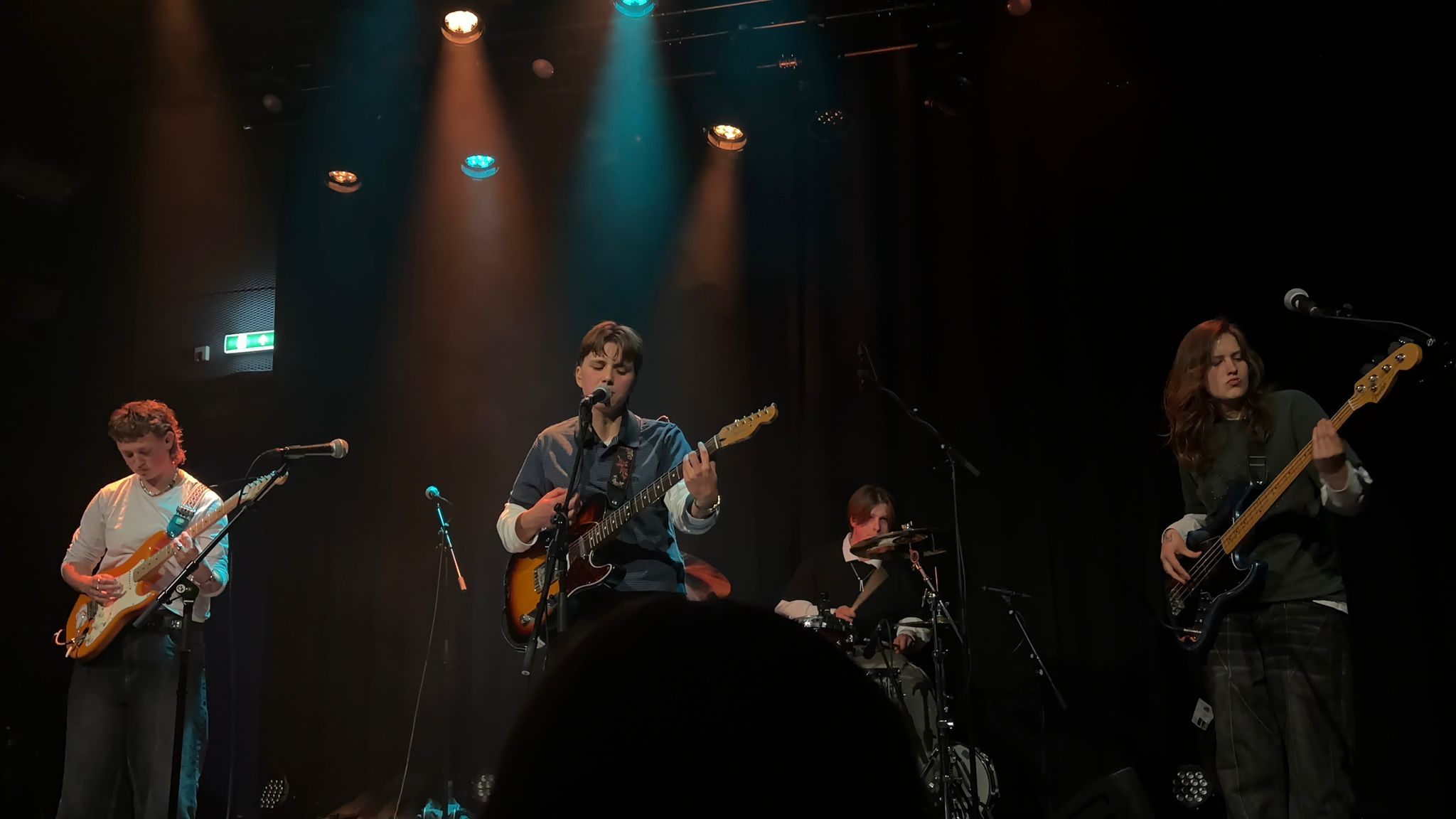 Band op podium met zanger-gitarist, tweede gitarist, drummer en bassist onder gekleurde spotlights